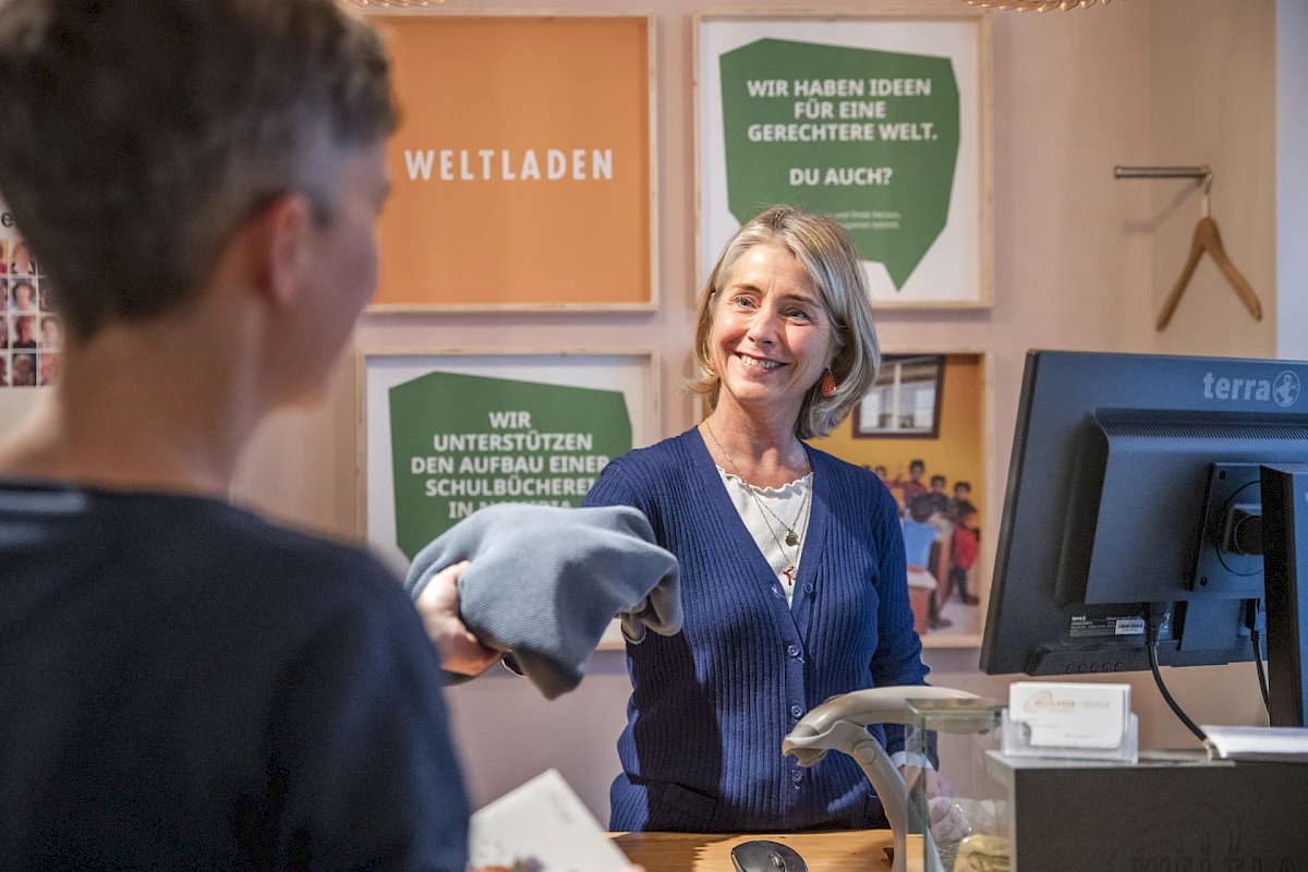 Weltladen-Mitarbeiterin verkauft einer Kundin Fair Fashion